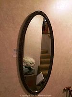 Full view of oval mirror against beige wall, showing overall size and shape.