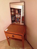 Wood telephone table with a single drawer seen from front and corner angle with mirror behind it reflecting bookshelves.