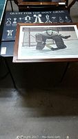Framed hockey goalie artwork on folding table, with black hockey trophy display board under it