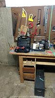 Tools and accessories laid out on wooden workbench with pegboard wall holding clamps and saws behind