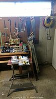 Wide view of workshop corner showing pegboard with hanging hand saws, clamps, extension cords, workbench with gloves, small containers with hardware, and other tools visible.