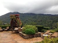 Mountain-view terrace with metal-framed wicker dining chairs, chaise loungers and stone planter box