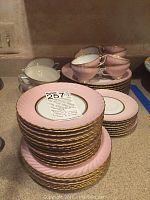 Full set of stacked plates and cups showing pink swirl pattern and gold trim.
