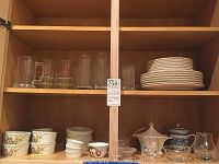 Shelved collection of assorted glasses, mugs, Nikko Woodberry plates, shallow bowls, various ramekins, serving pitcher, and small bowls.