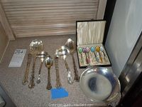 Group view of sterling serving utensils, bowl and boxed enameled spoons on countertop.