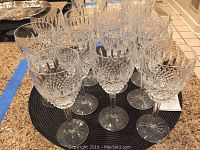 Group of 12 cut crystal wine glasses on black mat, angled view