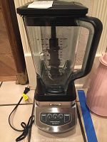 Full view of Ninja blender showing clear jar with markings, black lid, handle, base with cord visible.