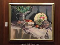 Framed still life painting showing a table with a green floral pitcher with flowers, bowl of fruit, decorative plate and covered dish, signed Carole Rhodes.