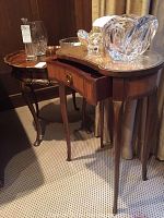 View of two side tables; one round with faux wood top, the other kidney-shaped with glass top and small drawer.