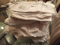 Stack of folded white table linens including lace edged pieces.