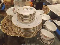 Stack of dinner and salad plates with cups and saucers at right