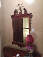 Full view of wood framed wall mirror with defined floral and scroll details, gold-tone decorative elements at the top, and hanging embellishments on the sides. Mirror size approximately 26x50 inches.