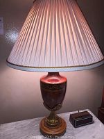 Photo showing one of the matching table lamps with wood and gold trimmed urn shaped base, topped with a beige pleated lampshade with gold rope trim.