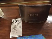 Brown leather Gucci sunglass case with gold Gucci embossing on front.