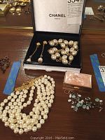 Chanel box open showing faux pearl necklace and matching drop earrings, multi-strand choker, pill box and silver-tone charm necklace.