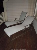 Two outdoor chaise lounges shown side by side on wooden deck, beige mesh fabric with metal frames.