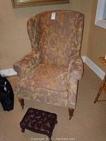 Photo of the upholstered paisley-patterned armchair with wooden legs and front casters.