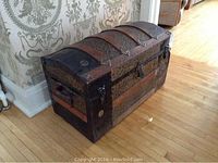 Full view of travel chest showing domed leather top with embossed floral pattern, metal and wood elements.