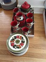 Photo showing full dish set including stacked plates, cups, saucers, teapot, creamer, and sugar container arranged on a wooden floor.