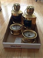 Overview of two brass lanterns, ship’s clock and barometer in cardboard tray