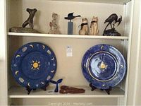 Shelf with two large blue decorative plates with sun and moon motifs and small figurines including glass whale tail and wooden items