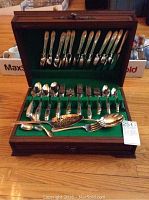 Front view of the open wooden case showing arranged cutlery including forks, spoons, and serving pieces on green felt.