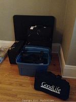 Wide shot of all items: a large black suitcase, black briefcases, blue Rubbermaid bin with eyeglass cases, large black foldable card table, and GoodLife tote bag.