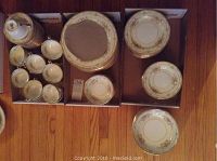 Overview of dinner plates, bowls, and smaller dishes in two cardboard boxes, showing stacked sets with floral and gold details.