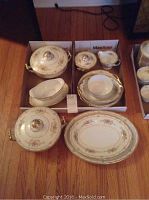 Full view of the collection showing various serving plates and bowls, gravy boat, creamer, sugar bowl with floral and gold pattern on wooden floor.