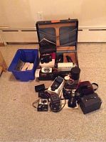 Overall assortment of cameras, flash, manuals and suitcase on carpeted floor