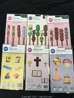Photo showing 6 Wilton chocolate molds for pretzels and lollipops in original packaging with various designs including gifts, hearts, graduation, religious symbols, and party themes.