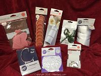 Display showing various packaged wedding accessories arranged on red fabric backdrop including bouquet wraps, bridal buttons, satin wraps, decorative doilies, monogram charms, bridal cake charms with ribbons, and a wedding shower game.