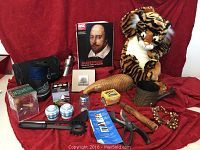 Overview photo showing all items together on red fabric including book, plush tiger, shaving kit, water bottle, kitchen items, and birdhouse gourd.