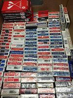 Photo showing numerous playing card packs stacked together, featuring varied brands and designs including red, blue, and white backs and several jumbo sized decks.