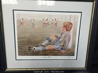Framed print showing a young boy sitting on grass watching a youth soccer game.