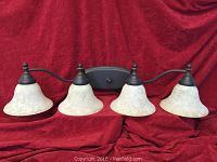 Photo of four-light vanity fixture with antique bronze metal frame and gold-tinted glass shades against red cloth background.