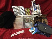 Photo shows a collection of 38 assorted music CDs and DVDs mostly Christian themed, unopened computer card game box labeled Hoyle with 33 card games for Windows, two new compact travel knapsacks in packaging, a market tote bag, green crocheted headband, and a new black velvet cap.