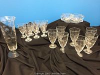Clear crystal stemware and cornflower pattern cream and sugar set on black fabric background as the full grouping.