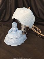 Blue milk glass Victorian-style lady table lamp with shell-shaped white milk glass lamp shade shown against dark background.