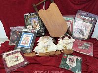Photo showing all items in the lot including the wooden sleigh, shoe stretchers, stitchery kits, and handmade angels arranged against a red backdrop.