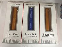 Photo of three power banks in their original packaging, two in orange and one in blue, showing front of boxes with device compatibility information.