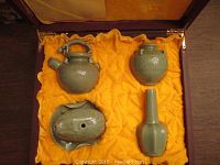 Four-piece celadonware Chinese tea set in a wood box with yellow fabric lining this set includes a teapot, a small vase, a bottle-shaped vase and a covered bowl or container