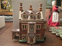 Front view of Dursley Manor building showing detailed facade, three chimneys, and holiday wreaths on windows with snow on roof edges.