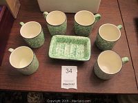 Six green marbled hand painted coffee cups arranged around a matching butter dish on a wooden table.