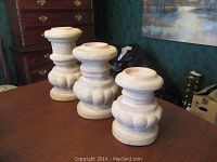 Front view of three carved white candle pillars positioned on a wooden table against a decorative wall and furniture.