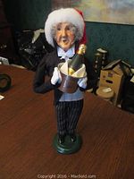 Full view of the butler caroler figurine standing on a green base, holding an ice bucket with champagne bottle, wearing a Santa hat.