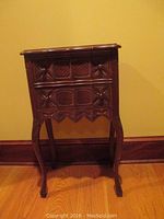 Full front view of the vintage wooden side table showing decorative carved drawer fronts and table legs.