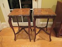 Pair of vintage side tables presented frontally on hardwood floor, showing overall wear and size.