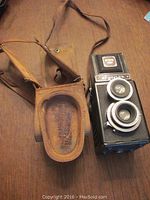 Vintage Argoflex camera next to worn leather carrying case on wood surface.