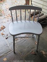 Blue country-style wooden bench with curved seat and spindle backrest, photographed outdoors on stone flooring with fallen leaves around